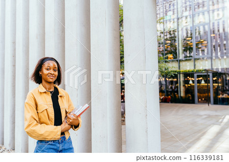 African girl with happy face learner studying on campus or walking outdoor with red book. Female student holding a book in a college. Education, school and people concept. 116339181