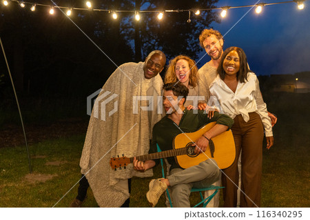 Friends having a fun outdoor gathering with music and string lights, creating a cheerful atmosphere 116340295