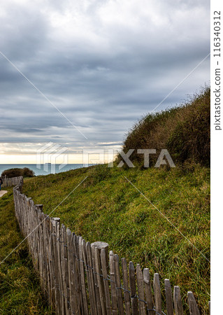 Enjoy a scenic coastal pathway with a wooden fence, grassy hills, and picturesque scenery Enjoy a scenic coastal pathway with a wooden fence, grassy hills, and picturesque scenery 116340312