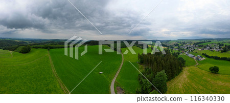 Experience the scenic view of green hills and a charming countryside village in this panorama Experience the scenic view of green hills and a charming countryside village in this panorama 116340330