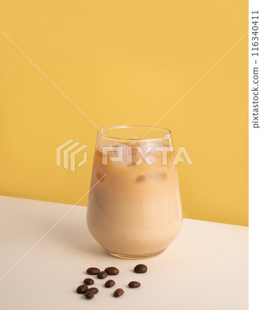 Iced coffee with milk in a glass with ice cubes and grains on a yellow background. Iced coffee with milk in a glass with ice cubes and grains on a yellow background. 116340411