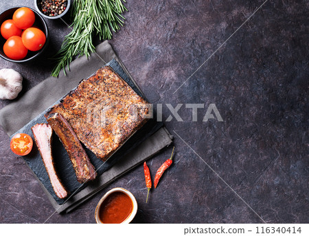 Juicy barbecue pork ribs with tomatoes, sauce and fresh herbs on a dark background. Juicy barbecue pork ribs with tomatoes, sauce and fresh herbs on a dark background. 116340414