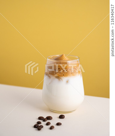 Dalgona coffee with milk in a glass with ice cubes and grains on a yellow background. Dalgona coffee with milk in a glass with ice cubes and grains on a yellow background. 116340417