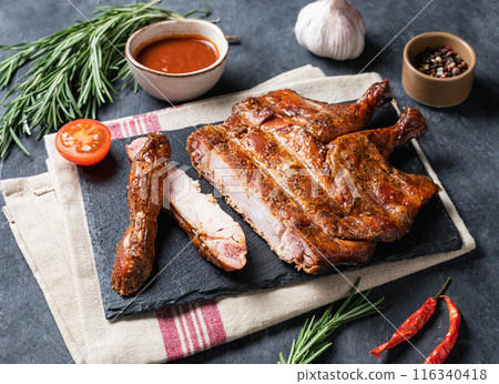 Roasted chicken legs bbq with sauce, tomato and fresh herb on a black slate on a dark background. Roasted chicken legs bbq with sauce, tomato and fresh herb on a black slate on a dark background. 116340418