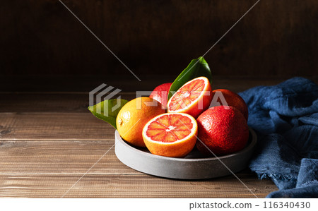 Juicy red oranges in a concrete bowl with a blue napkin on a dark wooden background. 116340430