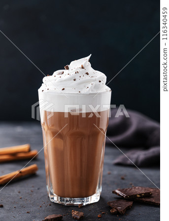 Hot chocolate with whipped cream and cinnamon in a tall glass on a dark background. Front view 116340459