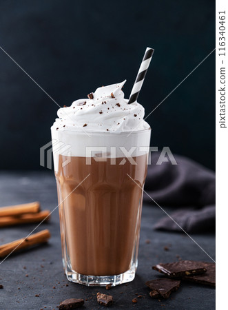 Hot chocolate with whipped cream, tube and cinnamon in a tall glass on a dark background. Hot chocolate with whipped cream, tube and cinnamon in a tall glass on a dark background. 116340461