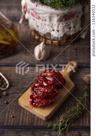 Sun-dried tomatoes in olive oil on a mini board with pepper, garlic and thyme in a rustic style. Selective focus, close-up. Sun-dried tomatoes in olive oil on a mini board with pepper, garlic and thyme in a rustic style. Selective focus, close-up. 116340532