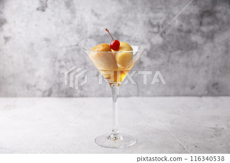 Neapolitan Rum baba (or baba au rum) in a martini glass with a cocktail cherry on a gray background. Small yeast cakes soaked in rum syrup. Traditional Italian pastry. Close-up, selective focus. 116340538