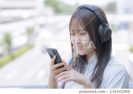 A high school girl using a smartphone while listening to music in the city A high school girl using a smartphone while listening to music in the city 116342069