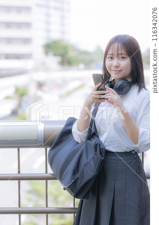 A high school girl using a smartphone while listening to music in the city A high school girl using a smartphone while listening to music in the city 116342076