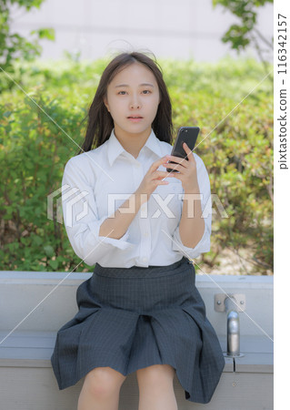 A high school girl sitting in the street and using a smartphone 116342157