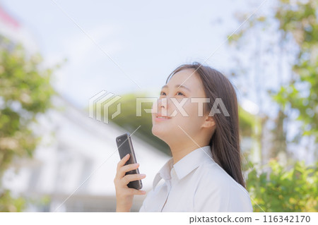 A high school girl sitting in the street and using a smartphone 116342170