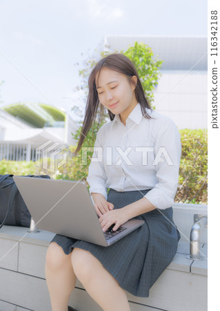 A high school girl sitting in the street and using a computer 116342188