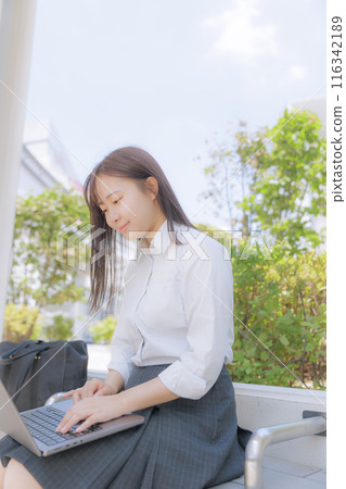 A high school girl sitting in the street and using a computer 116342189
