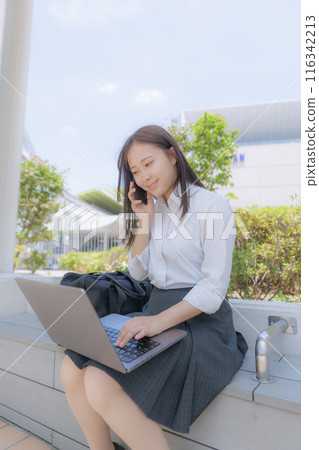 A high school girl sitting in the street and using a computer 116342213