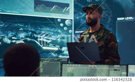 Special operations soldier allocating resources to different units based on mission needs, examines strategic data on a big screen in military control center. Marine corps troops. Camera A. 116342328