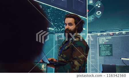 Army major monitoring data on a big screen in military command center, gathering information to execute a field mission. Captain leading his troops on a secret service defense operation. Camera B. 116342360