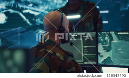 Male IT specialist operating on reconnaissance system to transmit real time data for new field mission, working in military command center. Telecommunications operator provides air support. Camera A. Male IT specialist operating on reconnaissance system to transmit real time data for new field mission, working in military command center. Telecommunications operator provides air support. Camera A. 116342390