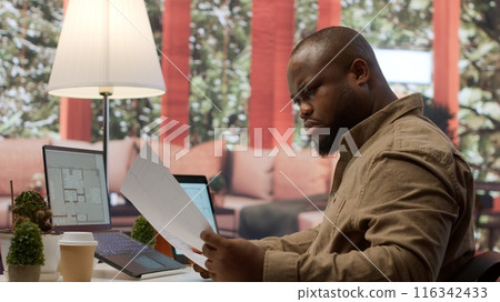 Businessman evaluating architectural blueprints for a modern office space, using strategic planning new commercial workspace leasing for his startup. Hunting for real estate property. Camera A. Businessman evaluating architectural blueprints for a modern office space, using strategic planning new commercial workspace leasing for his startup. Hunting for real estate property. Camera A. 116342433