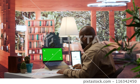 Entrepreneur examines financial statistics next to green screen at home desk, expert adviser calculating budget balance in order to expand business activity. Economic startup situation. Camera B. Entrepreneur examines financial statistics next to green screen at home desk, expert adviser calculating budget balance in order to expand business activity. Economic startup situation. Camera B. 116342450