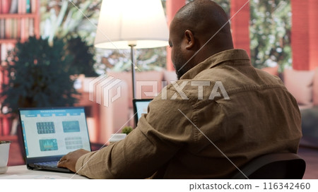 Startup entrepreneur looking into project details on laptop at his home setup, reviewing budget numbers and solving business tasks to achieve enterprise growth objectives. Camera A. Startup entrepreneur looking into project details on laptop at his home setup, reviewing budget numbers and solving business tasks to achieve enterprise growth objectives. Camera A. 116342460