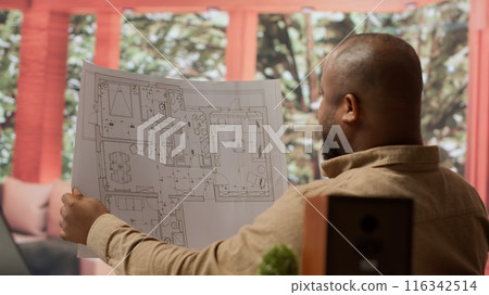 Corporate owner planning an office interior design renovation, reviewing blueprints and collaborating with contractors to create a modern workspace. Evaluating property sketches at home. Camera A. 116342514
