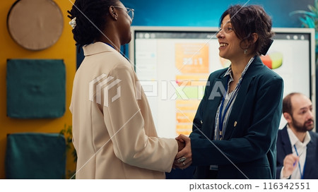 Project manager sharing insight about a new strategy with the new employee, shaking hands and welcoming her to the team in conference room. Coworkers in a new hire introductions meeting. Camera A. Project manager sharing insight about a new strategy with the new employee, shaking hands and welcoming her to the team in conference room. Coworkers in a new hire introductions meeting. Camera A. 116342551