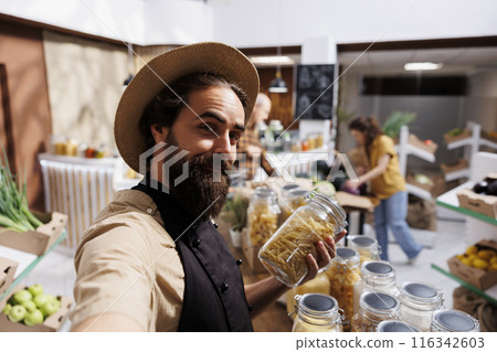 Zero waste shop entrepreneur using selfie camera on smartphone to promote environmentally conscious vegan products online. Ecofriendly supermarket owner making social media content for followers Zero waste shop entrepreneur using selfie camera on smartphone to promote environmentally conscious vegan products online. Ecofriendly supermarket owner making social media content for followers 116342603