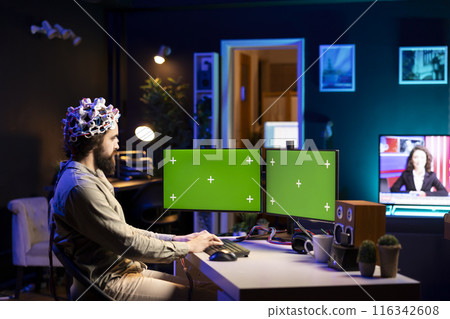 Software engineer with EEG headset starting mind upload on isolated screen multi monitor setup, trying to gain bionic powers. IT expert using high tech neuroscientific gear and mockup desktop PC 116342608