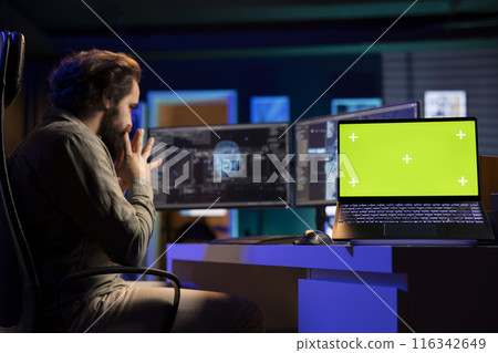 Green screen laptop next to programmer in home office staggered by AI gaining consciousness. Mockup notebook on desk next to computer scientist surprised by artificial intelligence turning autonomous 116342649