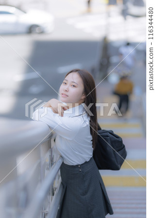 A high school girl standing in the street with a bag 116344480