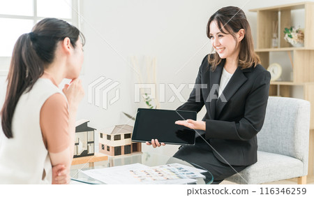 A businesswoman and a female customer, an architect, explaining about a new home while looking at blueprints, drawings, and a tablet A businesswoman and a female customer, an architect, explaining about a new home while looking at blueprints, drawings, and a tablet 116346259