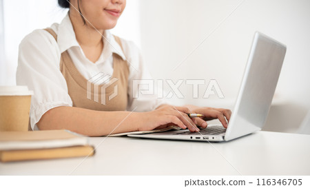 A cropped image of an Asian woman working on her laptop computer in a minimal white coffee shop. A cropped image of an Asian woman working on her laptop computer in a minimal white coffee shop. 116346705