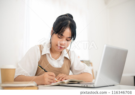 A young Asian female college student working remotely or studying an online class from a cafe. A young Asian female college student working remotely or studying an online class from a cafe. 116346708