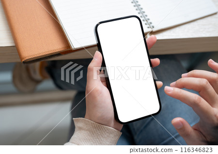 A close-up image of a woman sitting at an indoor table with her books and using her smartphone. 116346823