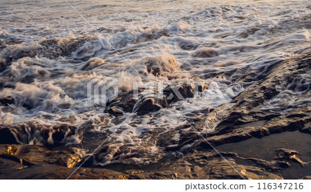 A large rocks surrounded by waves of the ocean A large rocks surrounded by waves of the ocean 116347216