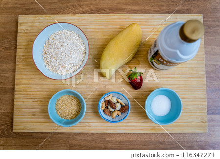 Cutting board with ingredients for preparing bowl of oats with strawberries and mango Cutting board with ingredients for preparing bowl of oats with strawberries and mango 116347271