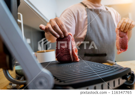 Chef at the kitchen preparing beef steaks on the home electric grill Chef at the kitchen preparing beef steaks on the home electric grill 116347765