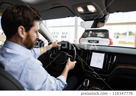 Businessman inside car dealership showroom test driving vehicle Businessman inside car dealership showroom test driving vehicle 116347776