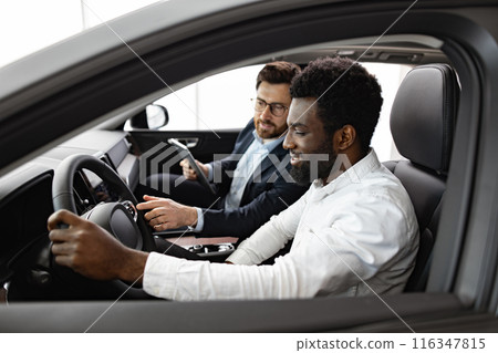 Caucasian car dealer inside vehicle with African American buyer Caucasian car dealer inside vehicle with African American buyer 116347815