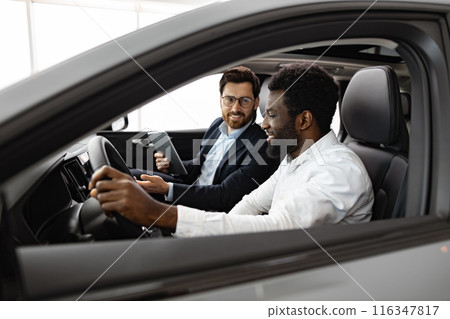Car dealer assisting customer with vehicle purchase inside car 116347817
