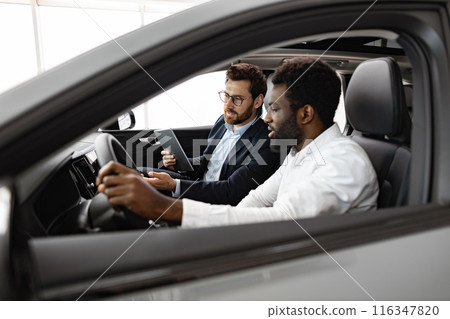 African American buyer consulting with Caucasian car dealer inside vehicle 116347820