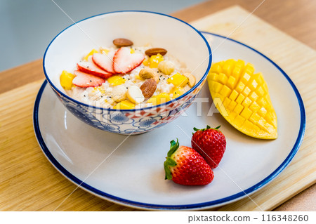 A bowl of oats with strawberries and mango arranged on a plate 116348260