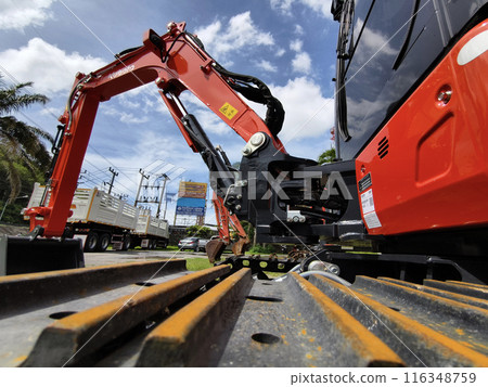 Red large excavators are stationed in a green field in front of a building 116348759