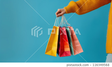 Close up of a woman's hand holding colorful shopping bags isolated on a blue background 116349568