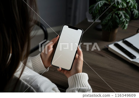 A woman holding a smartphone white screen on a wooden table 116349609