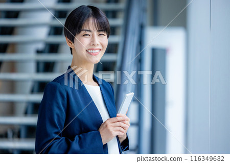 A young woman in a suit operating a smartphone in an office 116349682