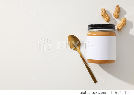 Peanut paste in a glass jar with a spoon, on a light background. Peanut paste in a glass jar with a spoon, on a light background. 116351101