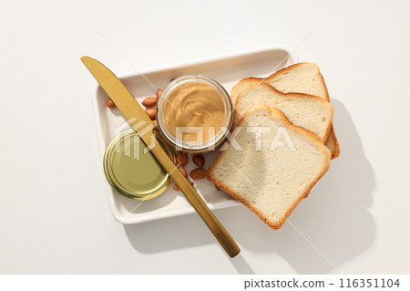 Peanut paste in a glass jar with a table knife, on a light background. Peanut paste in a glass jar with a table knife, on a light background. 116351104